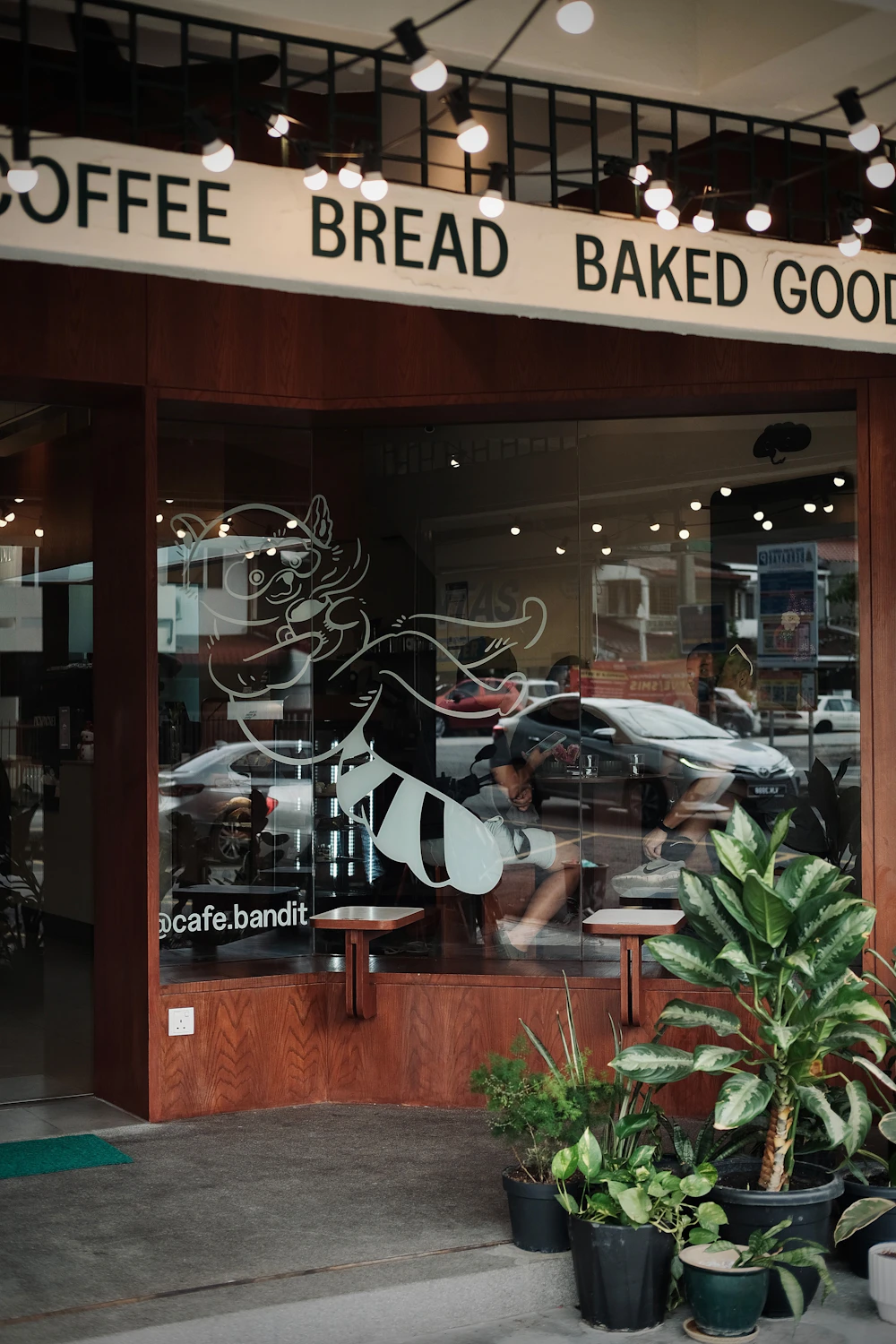 An independent cafe with a coffee and baked goods sign, windows and plants